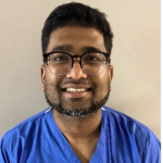 Chethram Nauth wearing glasses and blue scrubs, smiling