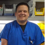 Mark Rusay wearing blue scrubs in lab, smiling